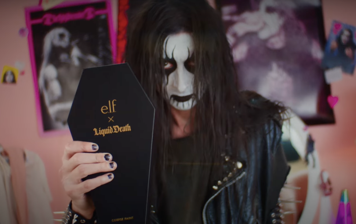 A person in goth makeup holds up a coffin-shaped package of makeup